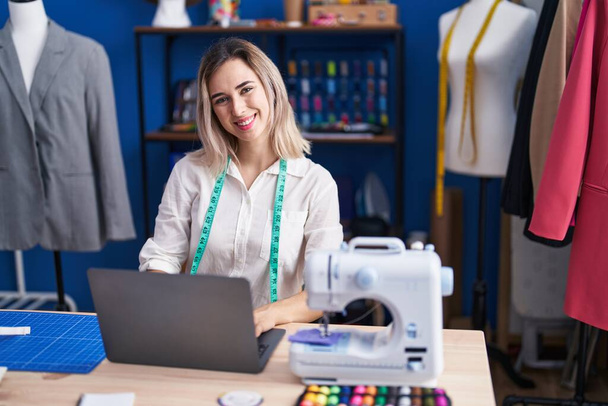 Jeune femme tailleur souriant confiant en utilisant un ordinateur portable à l'usine de vêtements - Photo, image