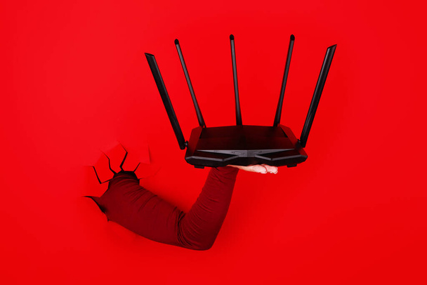 zwarte wifi router bij de hand over rode achtergrond - Foto, afbeelding