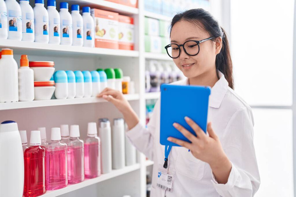 Young chinese woman pharmacist using touchpad working at pharmacy - Foto, Imagem
