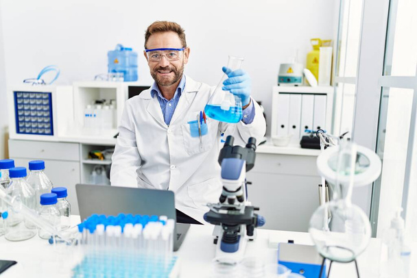 Hombre hispano de mediana edad vistiendo uniforme científico trabajando en laboratorio - Foto, Imagen