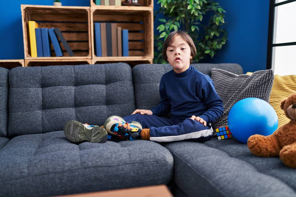Down syndrome kid relaxed sitting on sofa at home - Фото, зображення