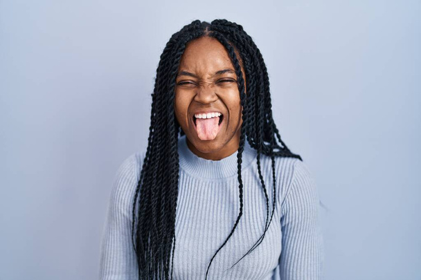 青い背景に立っているアフリカ系アメリカ人の女性は面白い表情で幸せ舌を突き出しています。感情の概念.  - 写真・画像