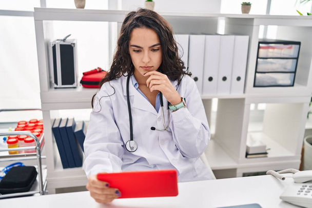 Mladá hispánka nosí lékařskou uniformu pomocí touchpad na klinice - Fotografie, Obrázek