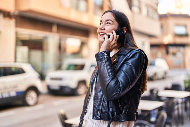 Młoda kobieta uśmiecha się pewnie rozmawiając na smartfonie na ulicy - Zdjęcie, obraz
