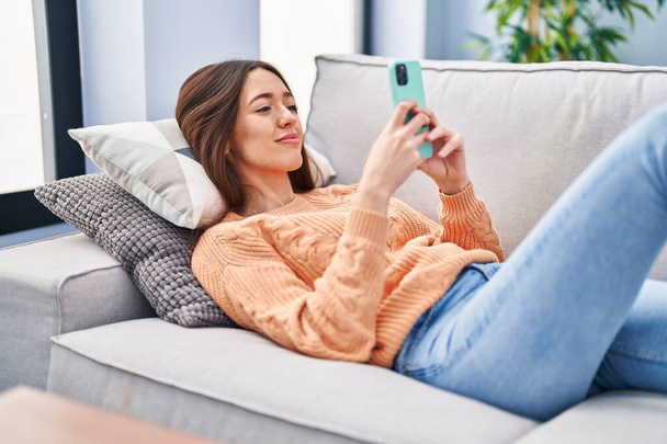 Jovem bela mulher hispânica usando smartphone deitado no sofá em casa - Foto, Imagem