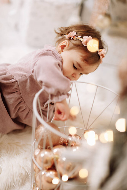 Suloinen vauva tyttö leikkii glitter joulu pallot metallilaatikossa, istuu valkoinen pehmeä matto olohuoneessa joulukuusi kotona. Käsite loma vietetään perheen kanssa. Hyvää uutta vuotta - Valokuva, kuva