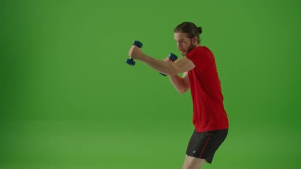 Side View.Young Motivated Bearded Fighter Doen Boksen oefeningen terwijl het dragen van rode sportkleding en blauwe Dumbells op een groen scherm, Chroma Key.Man Kickboksen en Self Defense Workout, Sport Concept. - Video
