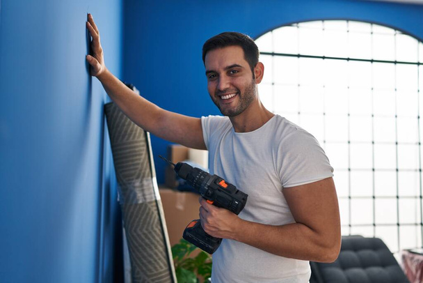 Nuori latino mies hymyilee luottavainen tilalla pora uudessa kodissa - Valokuva, kuva
