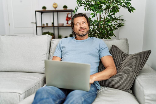Moyen âge caucasien homme souriant confiant en utilisant un ordinateur portable à la maison - Photo, image