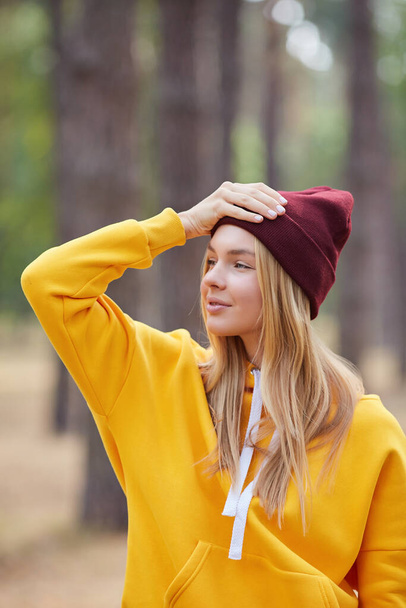 Closeup portrait of gorgeous young blonde Caucasian woman in knitted beanie in autumn in park. Young woman head shot, natural light, retouched, vibrant colors. - Фото, зображення