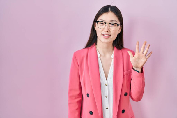 Čínská obchodní mladá žena nosí brýle ukazující a ukazující nahoru s prsty číslo pět a zároveň se usmívá sebevědomě a šťastně.  - Fotografie, Obrázek