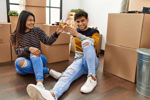 Mladý latinský pár přípitek s vínem sedí na podlaze v novém domově. - Fotografie, Obrázek