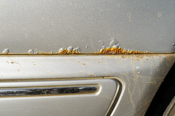 Corrosion on the body of a silver dirty car at the junction of the body elements. The process of physical deterioration and rusting of the car - Photo, Image