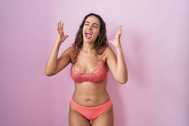 Jeune femme hispanique portant de la lingerie sur fond rose célébrant fou et fou de succès avec les bras levés et les yeux fermés hurlant excité. concept gagnant  - Photo, image