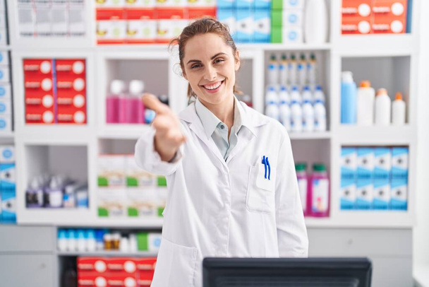 Молодая женщина фармацевт с приветственным выражением в аптеке - Фото, изображение