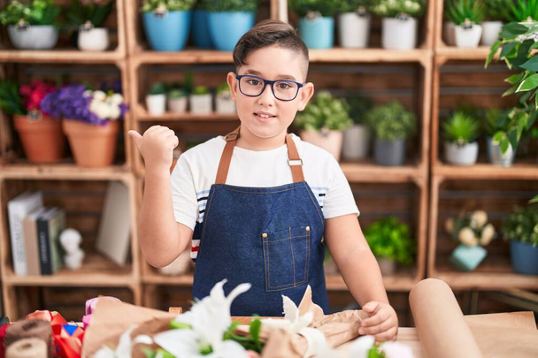 Young hispanic kid working at florist shop pointing thumb up to the side smiling happy with open mouth  - Foto, Imagem