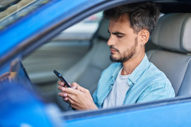 Young hispanic man using smartphone sitting on car at street - Fotografie, Obrázek