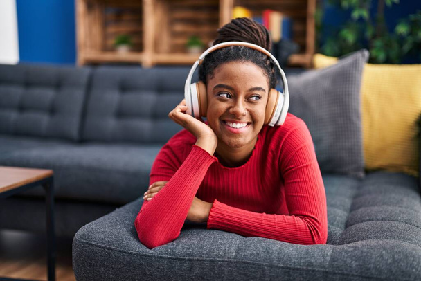 African american woman listening to music lying on sofa at home - Photo, image