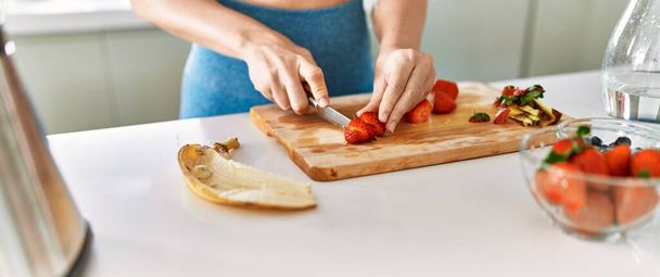 Молодая женщина режет клубнику на кухне - Фото, изображение