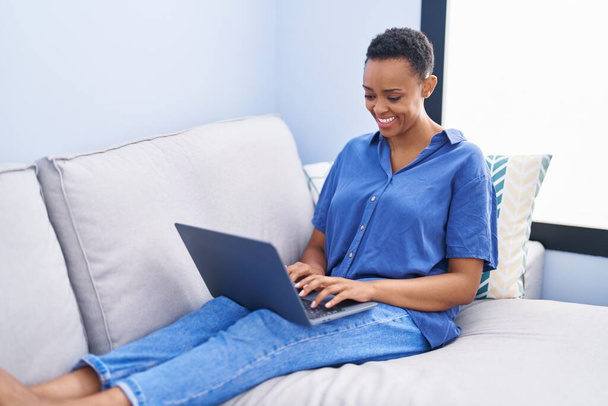 African american woman using laptop sitting on sofa at home - Foto, afbeelding