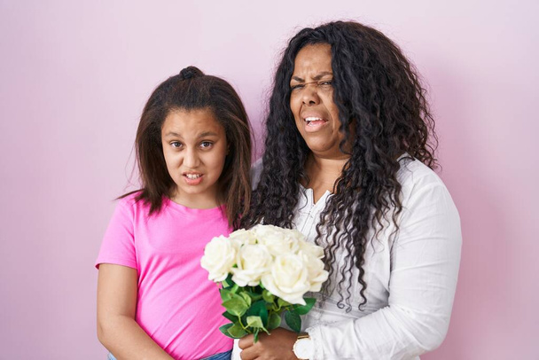 Anne ve küçük kızı ellerinde bir buket beyaz çiçek ve kafası karışık bir ifade tutuyorlar. şüphe kavramı.  - Fotoğraf, Görsel