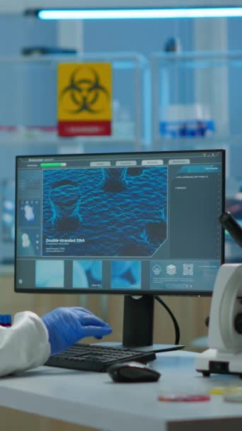 垂直ビデオ:現代の研究室で全体的にPCに入力してワクチン開発に取り組んでいる人科学者。ハイテク化学ツールを用いて医療研究室のウイルス進化を調べるチーム - 映像、動画