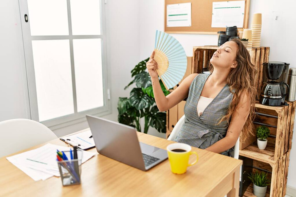 Joven hermosa mujer hispana trabajadora de negocios usando un ventilador de mano en la oficina - Foto, Imagen