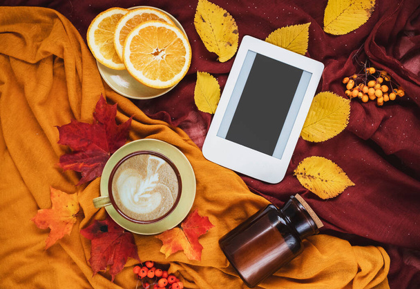 Φθινόπωρο σπίτι ζεστή σύνθεση με κίτρινο και μπορντό κουβέρτες, φλιτζάνι καφέ, φέτες πορτοκαλιού, κόκκινα και κίτρινα φύλλα και e-book με χώρο αντίγραφο. Πρότυπο φθινοπωρινής σεζόν για θηλυκό blog social media. - Φωτογραφία, εικόνα
