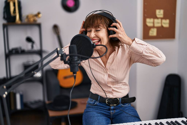 Mulher de meia idade músico sorrindo canção cantando confiante no estúdio de música - Foto, Imagem