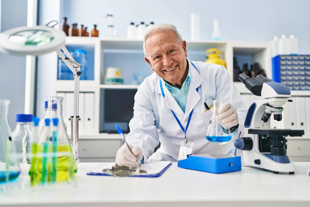 Senior man draagt wetenschapper uniform meten vloeistof in het laboratorium - Foto, afbeelding