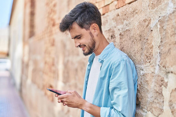 Jeune homme hispanique souriant confiant en utilisant un smartphone dans la rue - Photo, image