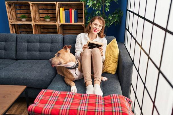 Young caucasian woman looking photo sitting on sofa with dog at home - Foto, Bild