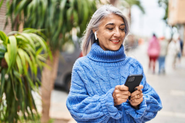 Седовласая женщина средних лет, уверенно улыбающаяся, слушая музыку на улице - Фото, изображение