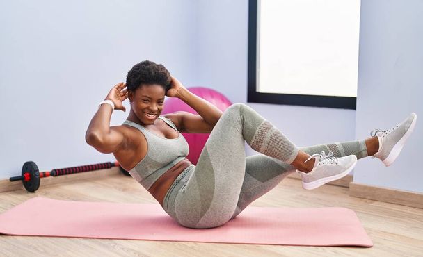Αφροαμερικανή γυναίκα χαμογελώντας με αυτοπεποίθηση κατάρτισης abs άσκηση στο αθλητικό κέντρο - Φωτογραφία, εικόνα