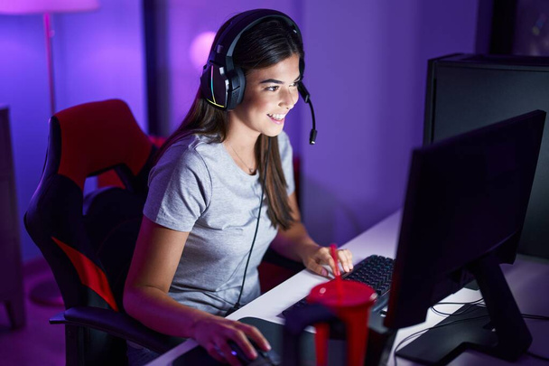 Young beautiful hispanic woman streamer playing video game using computer at gaming room - Foto, afbeelding