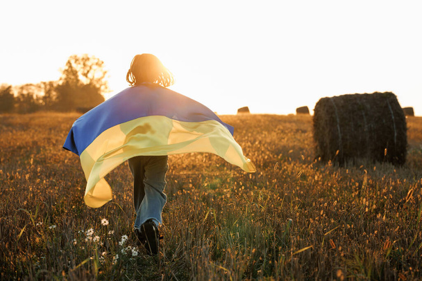 Little Girl with flag of Ukraine running on the field. Patriotic Girl Flying Ukrainian Flag, Ukraine August 24 banner. Kid standing outdoors at sunset. International day of democracy concept. Flag Day - Фото, изображение