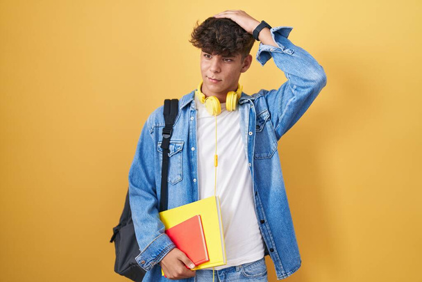 Hispanic teenager wearing student backpack and holding books confuse and wondering about question. uncertain with doubt, thinking with hand on head. pensive concept.  - Foto, imagen