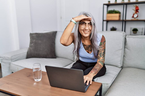 Siwowłosa kobieta w średnim wieku, używająca laptopa w domu, bardzo szczęśliwa i uśmiechnięta, patrząca z daleka. koncepcja wyszukiwania.  - Zdjęcie, obraz