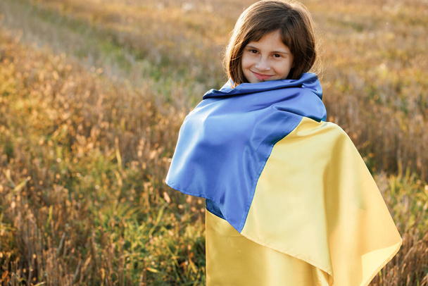 Portrait of teenager girl looking at camera wearing blue and yellow flag of Ukraine. Flag of Ukraine in hands of ukrainian girl. War in Ukraine. Support for Ukraine - Photo, image