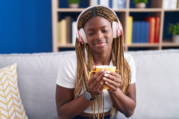 Mujer afroamericana escuchando música tomando café en casa - Foto, imagen