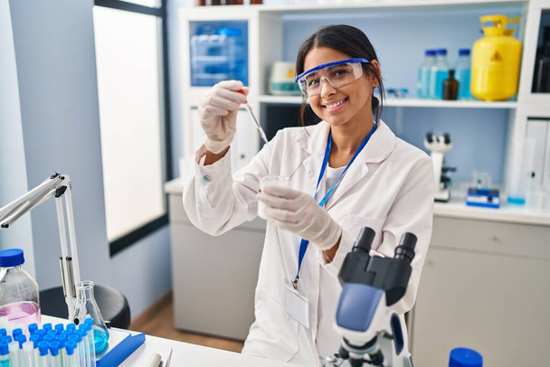 Young latin woman wearing scientist uniform using pipette at laboratory - Photo, Image