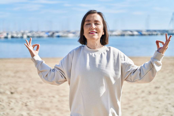 Middle age woman smiling confident training yoga at seaside - Foto, immagini
