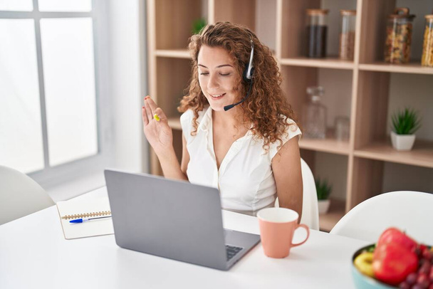 Young caucasian woman wearing call center agent headset working from home doing ok sign with fingers, smiling friendly gesturing excellent symbol  - Фото, зображення