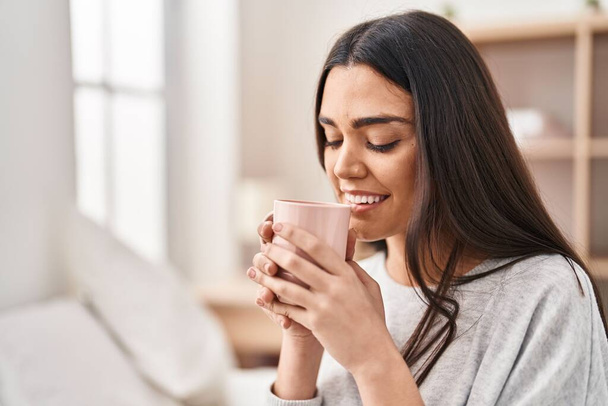 Fiatal spanyol nő iszik csésze kávét ül az ágyon a hálószobában - Fotó, kép