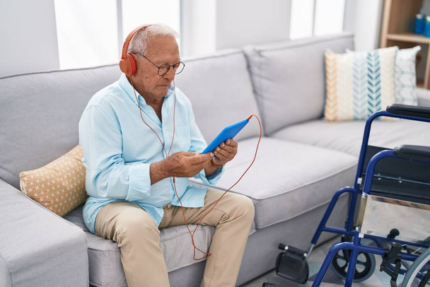 Älterer grauhaariger Mann schaut Video auf Touchpad und sitzt zu Hause auf Sofa - Foto, Bild