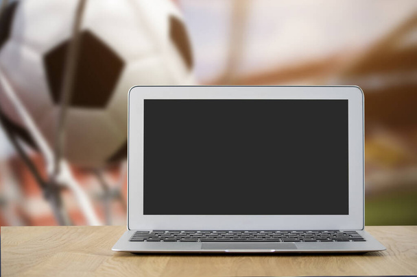 Um laptop com uma tela em branco com um estádio de futebol embaçado no fundo. Cole sua própria imagem na tela para uma imagem personalizada - Foto, Imagem