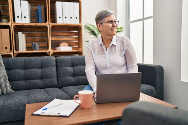 Psicólogo mulher de meia idade usando laptop sentado no sofá no centro de pyschology - Foto, Imagem