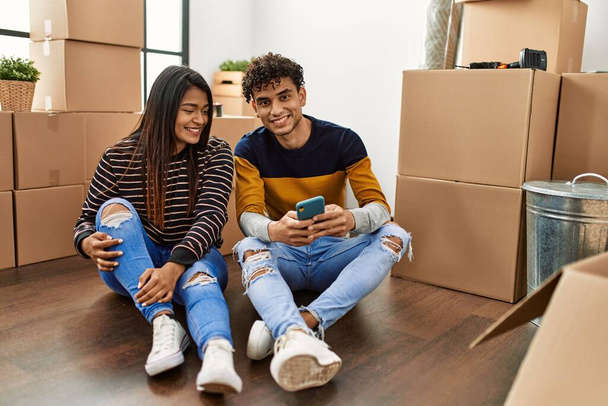 Fiatal latin pár használ okostelefon ül a padlón az új otthon. - Fotó, kép