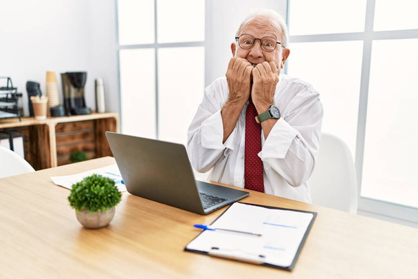 Hombre mayor que trabaja en la oficina usando computadora portátil riendo y riéndose avergonzado cubriendo la boca con las manos, chismes y concepto de escándalo  - Foto, Imagen