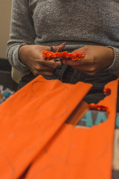 Μεξικάνες κόβουν λωρίδες πορτοκαλί χαρτιού για να φτιάξουν λουλούδια cempasuchil για την Ημέρα των Νεκρών προσφορών. - Φωτογραφία, εικόνα